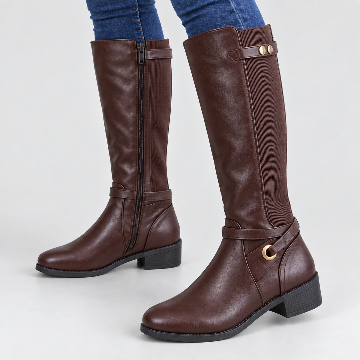 Brown tall riding boots with stretch panel and ankle ring worn by a model against a light grey studio background